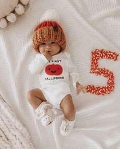 a baby wearing a knitted hat and bodysuit with the number five on it