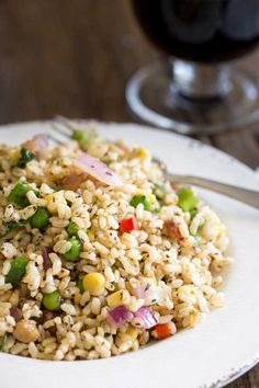 a white plate topped with rice and veggies next to a glass of wine