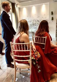 two women in red dresses are sitting on chairs and one man is standing behind them