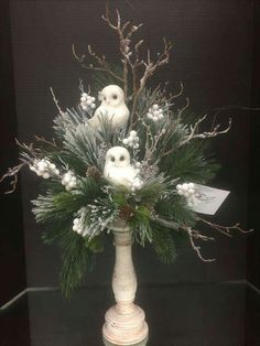 a white vase filled with lots of snow covered plants and birds sitting on top of it