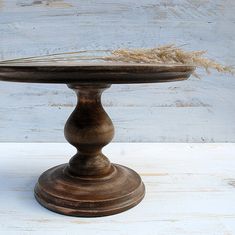 an old wooden cake stand on a white wood table with dried grass in the center