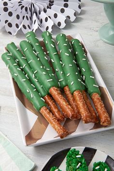 green and white dessert sticks with sprinkles arranged on a plate next to cupcakes