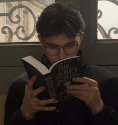 a young man reading a book in front of a window