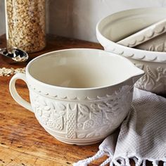 two white bowls sitting on top of a wooden table next to a spoon and bowl