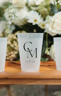 three plastic cups sitting on top of a wooden table next to white flowers and greenery