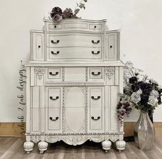 a white dresser sitting next to a vase filled with flowers