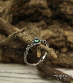 a close up of a ring on top of a tree branch with a green stone in the middle