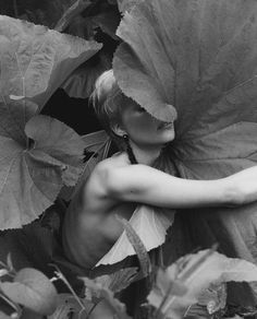 black and white photograph of a naked woman surrounded by large leafy plants in the woods