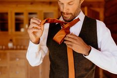 a man wearing a vest and tie tying his orange necktie in front of him