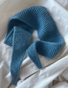 a blue knitted headband laying on top of a white bed sheet with pillows