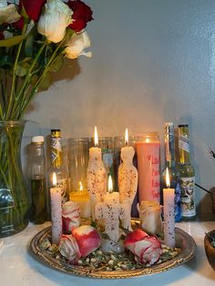 candles are lit on a tray with roses in the center and other items around it