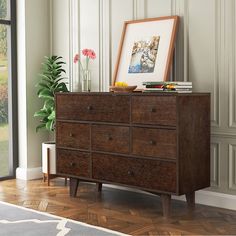 a wooden dresser sitting in front of a window next to a vase with flowers on it