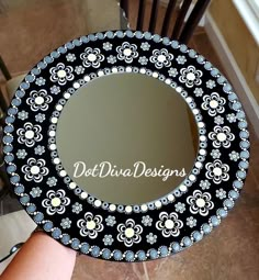 a person holding up a decorative mirror with the words dot dura designs on it