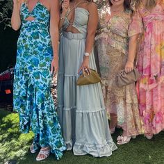 four women in dresses standing under an umbrella