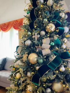 a decorated christmas tree with gold, silver and green ornaments on it in a living room