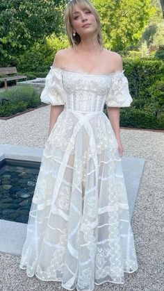 a woman standing in front of a pond wearing a white dress