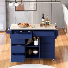 a blue kitchen island with drawers and bottles on it in front of a dining room table