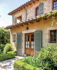 a house with green shutters on the front and side windows, surrounded by greenery