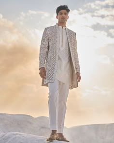 a man standing on top of a snow covered hill wearing a white suit and tie