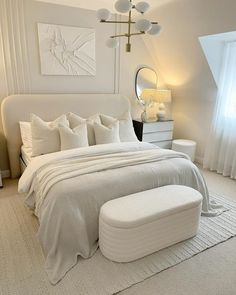 a white bedroom with a large bed and ottoman