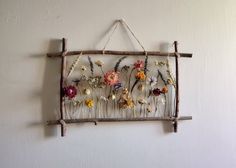 a wall hanging made out of branches with flowers attached to the top and bottom part