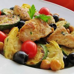 a white plate topped with chicken, zucchini and tomatoes next to olives