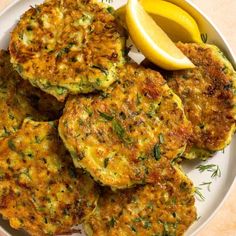 some crab cakes are on a plate with lemon wedges