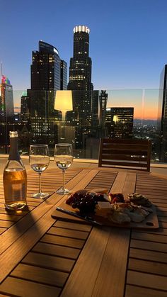 two glasses of wine and some food on a wooden table in front of a cityscape