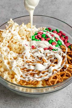 a glass bowl filled with cereal, marshmallows and pretzels being drizzled with white icing