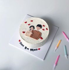 a birthday cake with two people on it and some crayons next to it