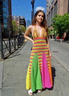 a woman in a multicolored dress standing on the sidewalk with her hands on her hips