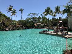 a large swimming pool surrounded by palm trees and people sitting at tables in the water