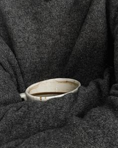 a person wearing a gray sweater and holding a white bowl in their lap with one hand