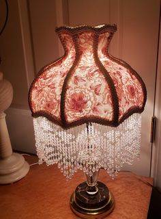 a lamp that is sitting on top of a table with beads hanging from it's sides