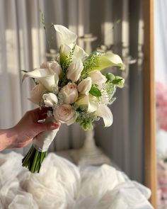 a person holding a bouquet of flowers in front of a bed with white linens