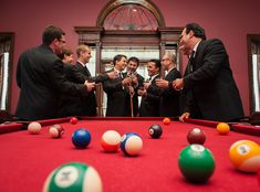 a group of men in suits standing around a pool table with billiard balls on it