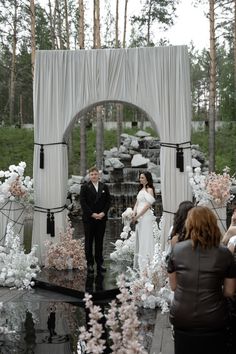 a bride and groom standing in front of an outdoor waterfall with flowers on the ground