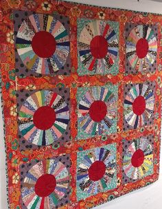 a quilted wall hanging on the side of a white wall with red and green circles