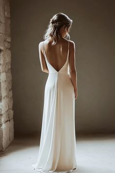 A woman stands with her back facing the camera, wearing a long, elegant white dress with a deep V-back and thin straps. Her hair is styled in loose waves and the setting is softly lit with muted tones. Elegant Minimal Wedding Dress, Dress White Elegant, Minimalist Bridal Gown, Silk Spaghetti Strap Wedding Dress, Vintage Inspired Wedding Dress, Simple Wedding Dress, Tiered Wedding Dress, 2 Piece Wedding Dress, Spaghetti Strap Wedding Dress