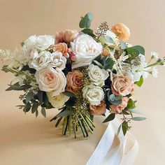 a bouquet of white and peach flowers with greenery on the side is wrapped in a white ribbon