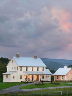 a large white house sitting in the middle of a lush green field under a cloudy sky