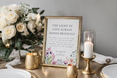 a table topped with white flowers and candles next to a framed sign that says the light of love always shines brightly