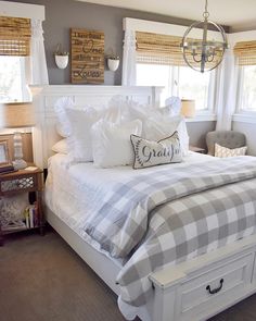 a white bed sitting in a bedroom next to two windows and a lamp hanging from the ceiling