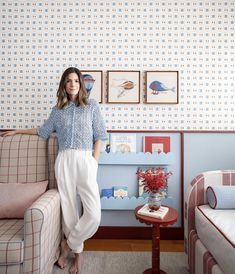 a woman standing in front of a couch next to a wall with pictures on it