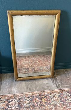 a mirror sitting on top of a wooden floor next to a blue wall and rug