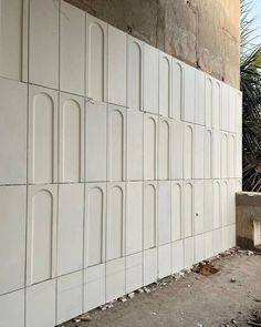 a wall made out of white tiles next to a palm tree