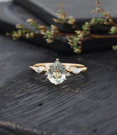 an engagement ring with a pear shaped aquamarinee stone and diamond accents on a wooden surface