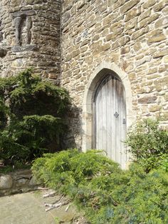 an old stone building with a wooden door in the center and bushes around it, on a sunny day