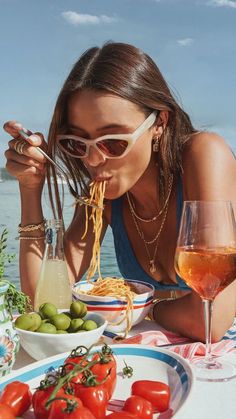 a woman sitting at a table with plates of food and drinks in front of her