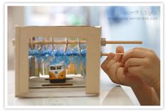 a hand holding a stick over a miniature model of a bus in a frame with blue streamers